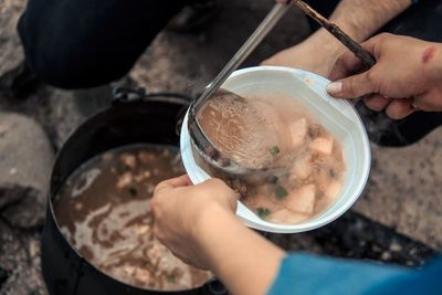 Cropped hand of person serving soup to friend at campsite