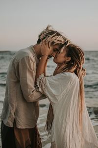 Young couple standing at sea shore against sky