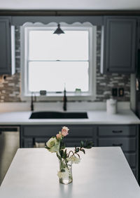 White kitchen countertop with flowers and vase and window in backgroun