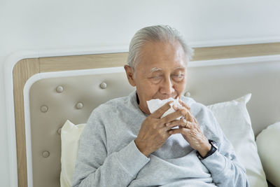 Man holding tissue paper while sitting on bed at home