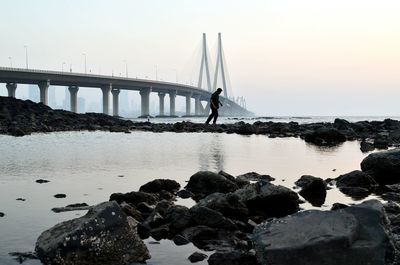 Man walking on rocks amidst sea against bandraworli sea link