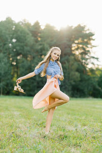 Smiling young woman in casual clothes strolls through the park. she is holding shoes in her hands