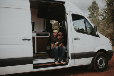 Happy girlfriend embracing boyfriend while sitting in motor home at forest