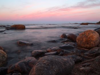 Rocks at sea shore against sky during sunset