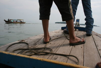 Low section of man standing on boat in sea