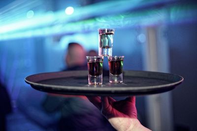 Cropped hand of waiter holding tray with alcohol shot glasses at nightclub