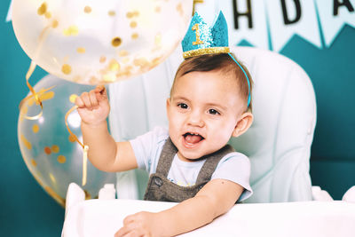 Cute baby boy holding balloon on high chair in birthday party