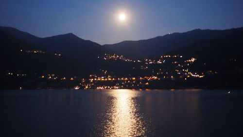 Illuminated city by sea against sky at night