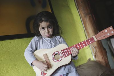 Portrait of girl making face while playing guitar at home