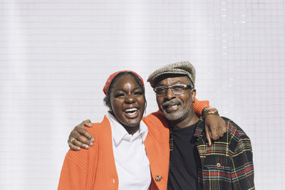 Portrait of cheerful father and daughter with arms around against wall during sunny day