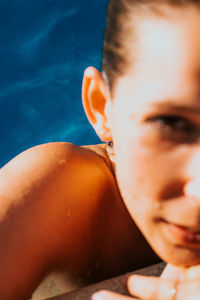 Blurred cropped close up woman with wet hair looking at camera relaxing by the poolside on sunny day