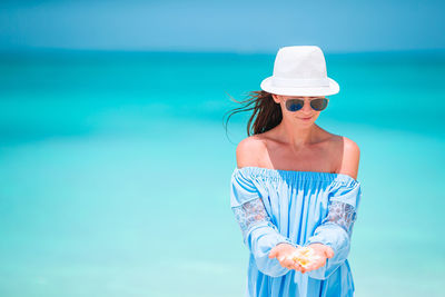 Midsection of woman wearing sunglasses standing against blue sea