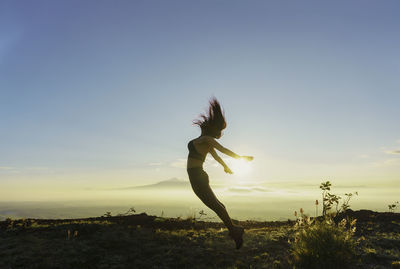 Full length of woman with arms raised standing against sky during sunset