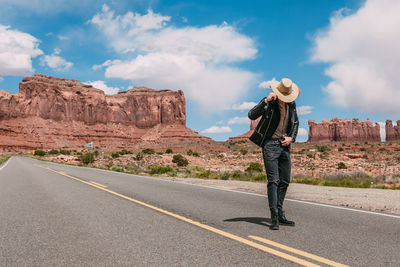 Man standing on rock by road against sky