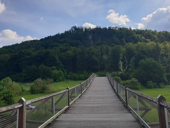 Footbridge amidst trees against sky