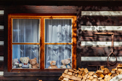 Wooden window with teddy bears and pille of wood outside