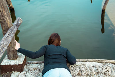 Rear view of woman bending on surrounding wall against lake