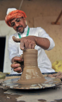 Midsection of potter making earthenware on pottery wheel at workshop