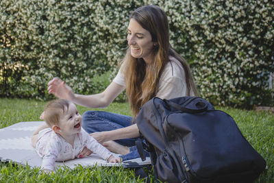 Portrait of young woman and cute baby sitting on field