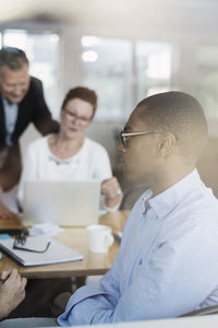 Businessman sitting while colleagues using laptop at board room