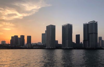 Sea by buildings against sky during sunset in city