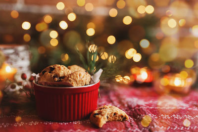 Red festive bowl full with christmas cookies, blurred christmas fir tree lights