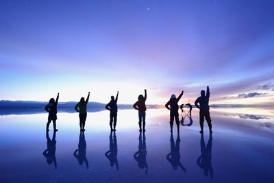 Silhouette friends gesturing at beach against sky during sunset