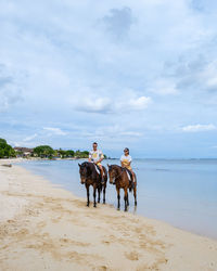 Man and woman sitting on horse at beach