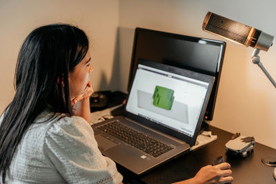 Rear view of young businesswoman sitting at desk, using laptop and 3d design software