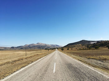 Empty road leading towards mountains against clear blue sky