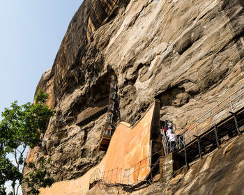 Low angle view of people on rock against sky