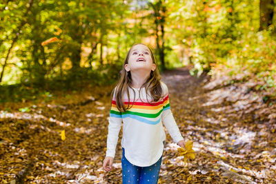 Cute girl looking up while standing in forest during autumn