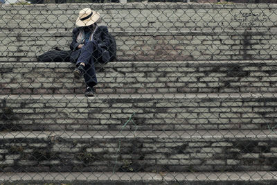 Full length of man sitting on steps seen through fence