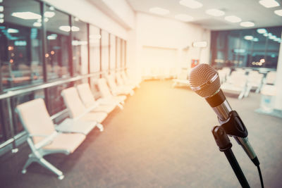 Close-up of microphone with empty chairs in illuminated room