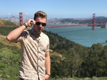Portrait of young man wearing sunglasses while standing against golden gate bridge