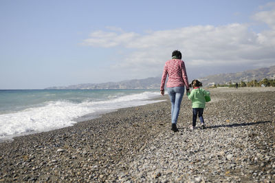 Rear view of mother and daughter walking on shore at beach