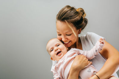 Mother holding daughter against gray background