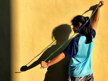 Rear view of girl holding jump rope against wall