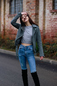 Full length of young woman standing on street against wall