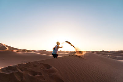 Man blowing sand in desert against sky