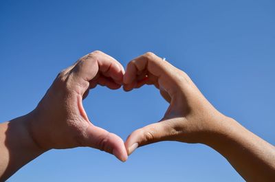 Low angle view of couple making heart shape against clear blue sky