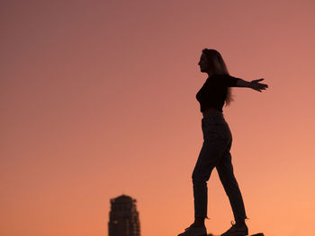 Silhouette woman with arms outstretched standing against orange sky