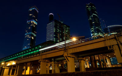 Blurred motion of train on railway bridge by skyscrapers in city at night