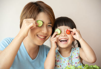 Portrait of smiling mother and daughter holding food over eyes