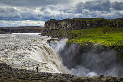 Scenic view of waterfall against cloudy sky