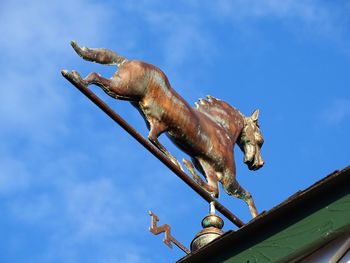 Low angle view of horse sculpture on roof against sky