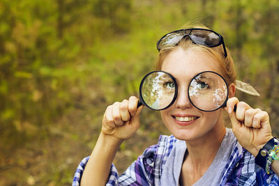 Close-up portrait of young woman holding magnifying glasses in forest
