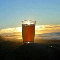 Close-up of beer glass against sky during sunset