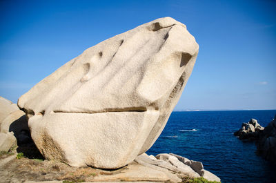 Close-up of rock by sea against clear blue sky