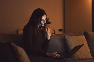 Young woman using laptop while sitting on sofa at home